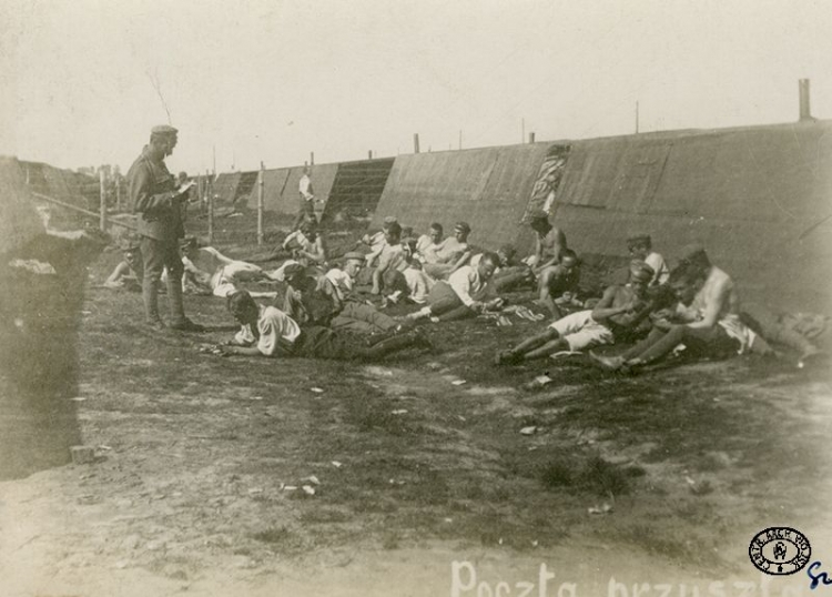 Internowani legioniści podczas czytania poczty przed barakami w obozie internowanych. Szczypiorno. 1917 r. Źródło: CAW